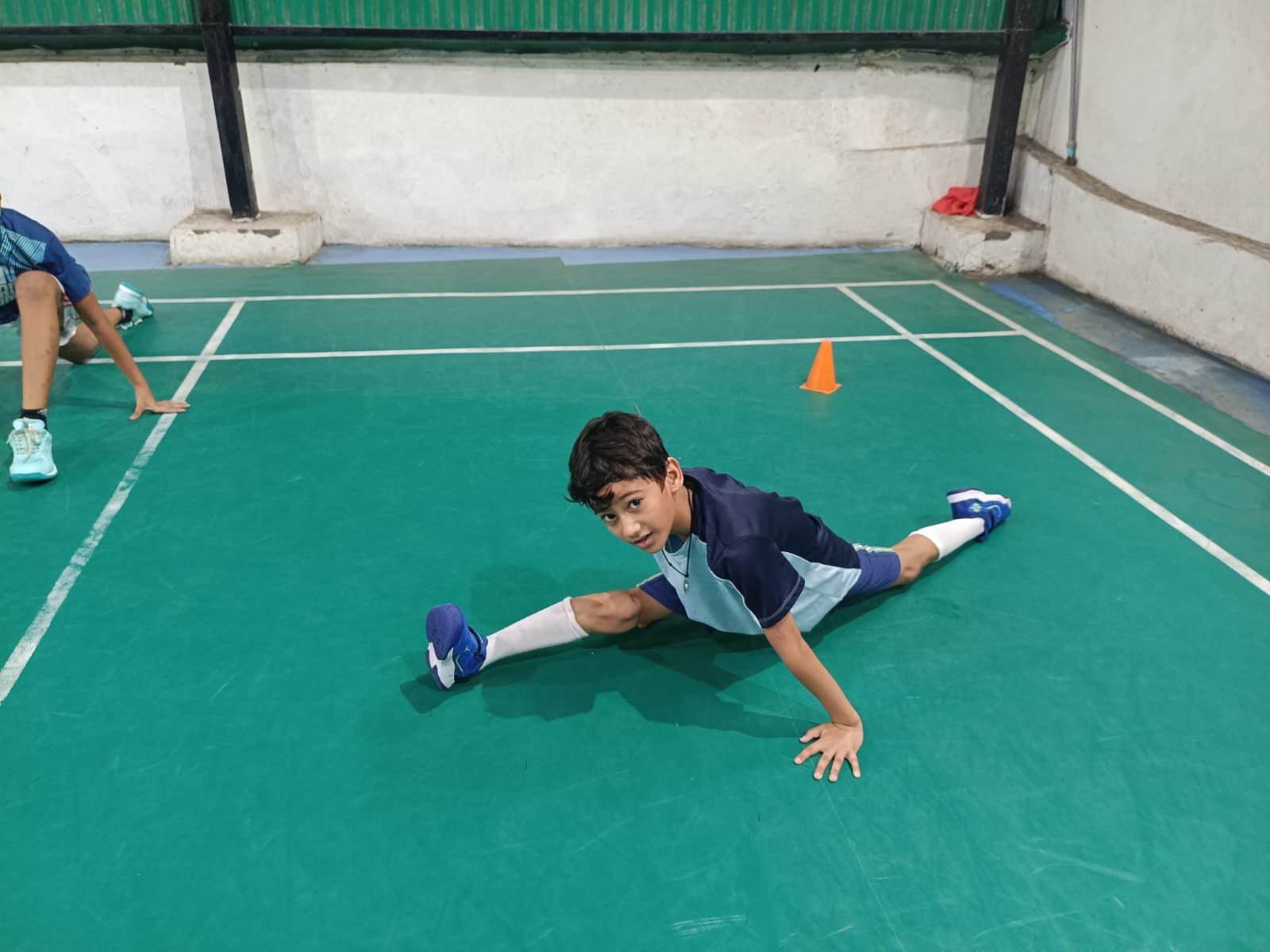 A junior player holding a middle split stretch on court at SSAB